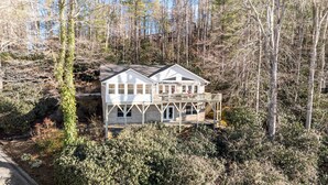 Une maison à deux étages, dotée d’un balcon et d’une terrasse, entourée d’une forêt dense.