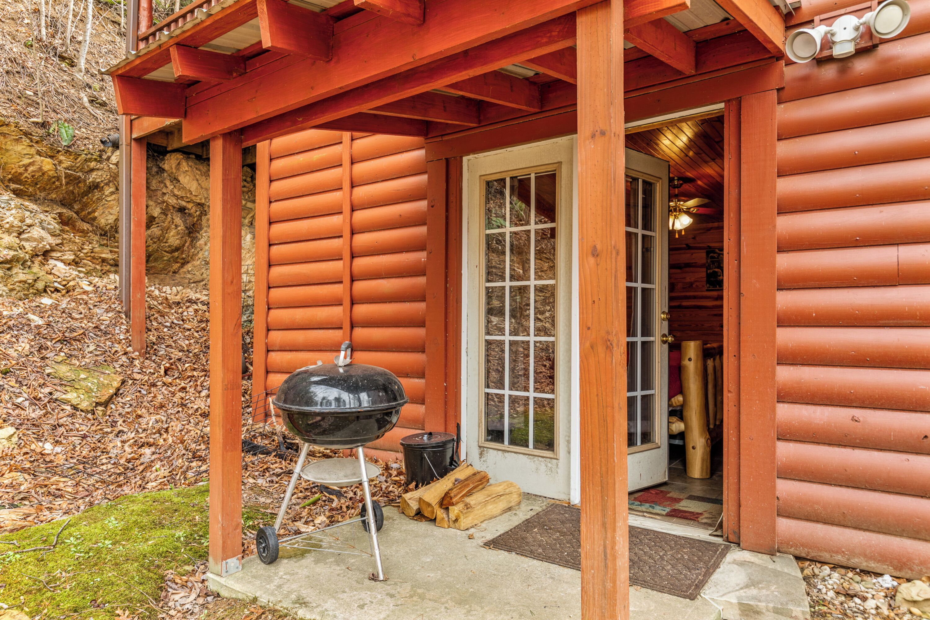 A wooden cabin with a covered porch, a grill, and a door leading inside.