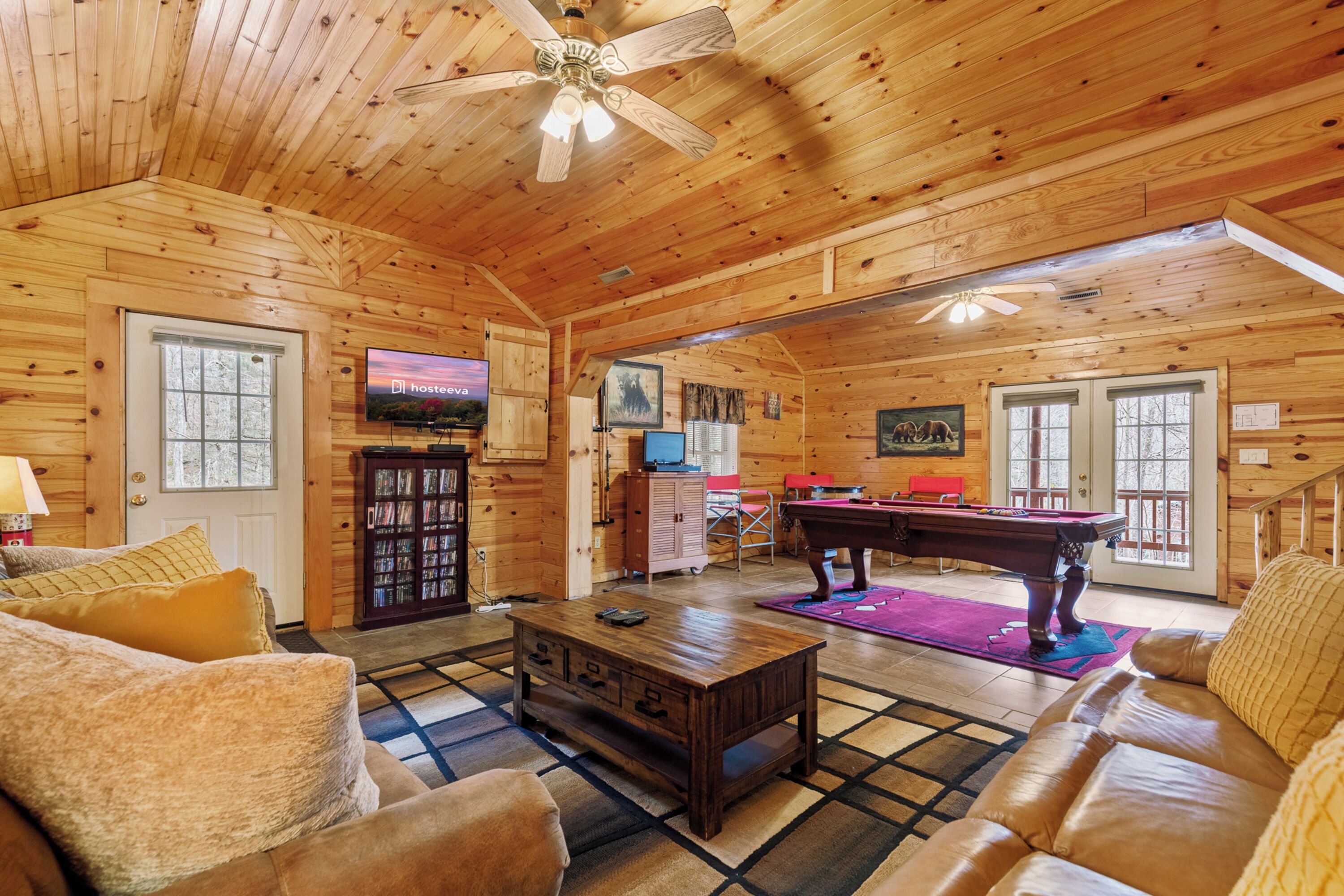 A wooden cabin interior with a living room, television, pool table, and a ceiling fan.