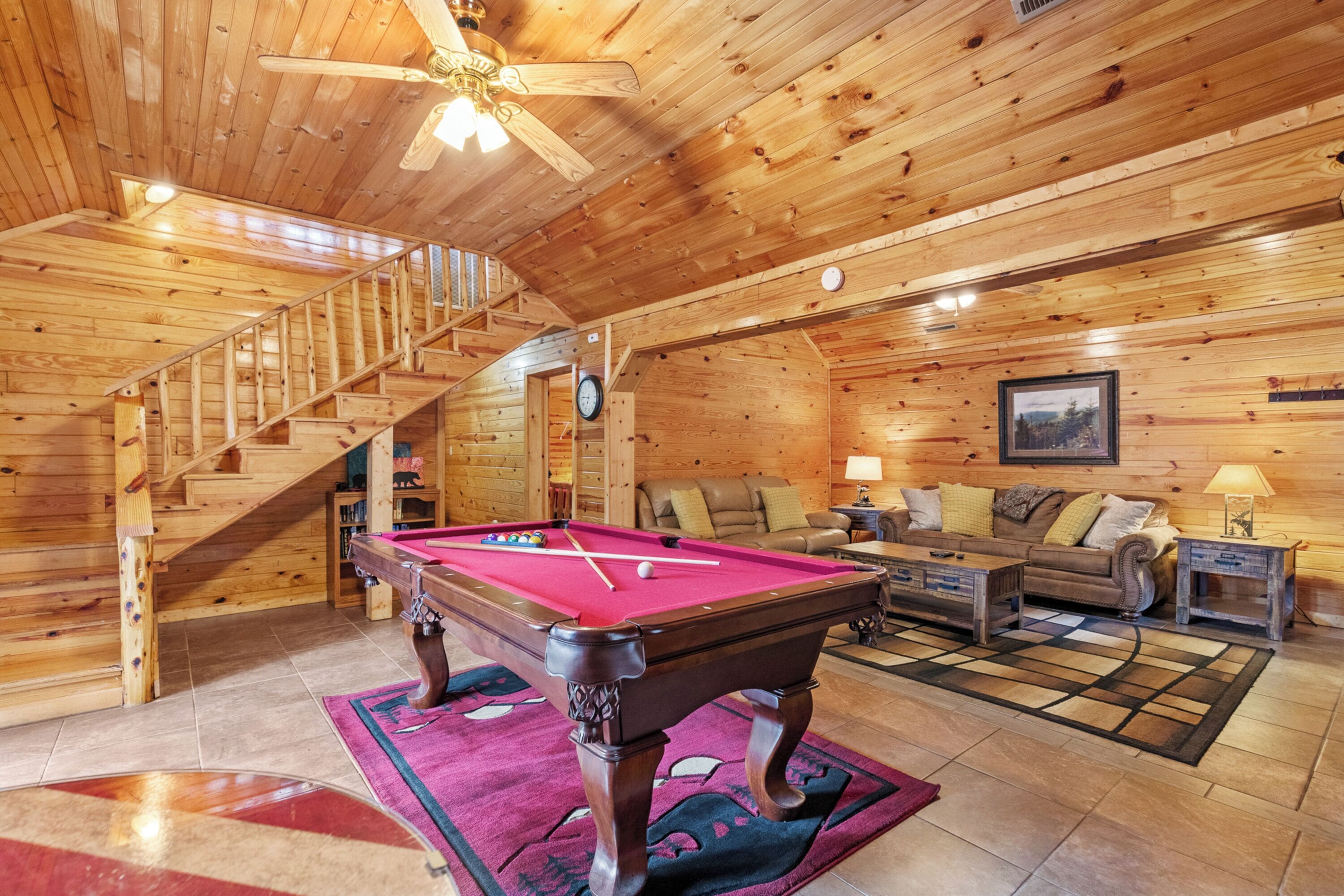Ein Holzinterieur mit Poolbillard, einer Couch und einer Treppe.