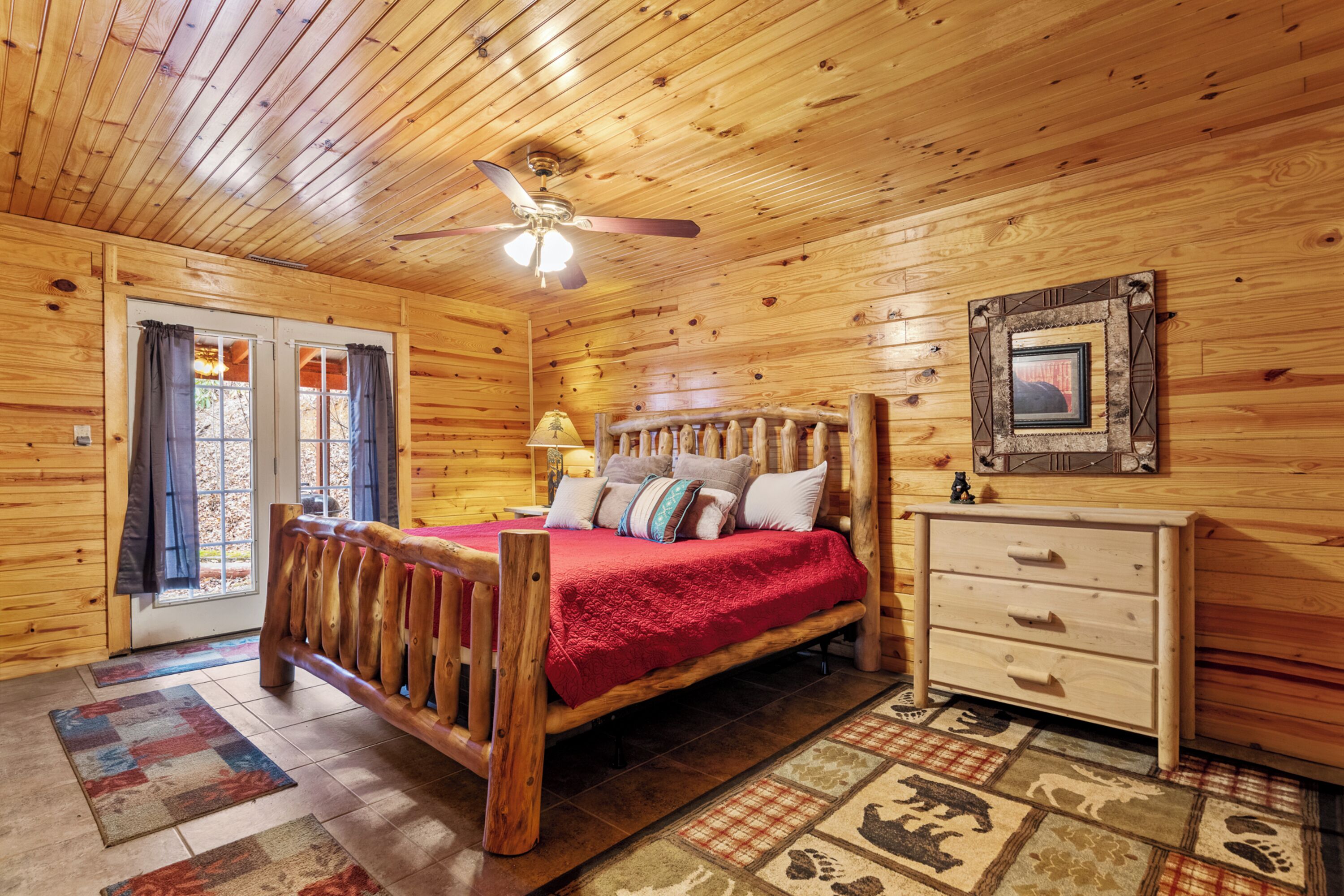 A wooden cabin bedroom with a bed, a dresser, and a ceiling fan.