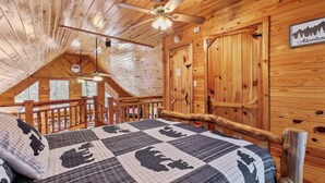 A cozy log cabin bedroom with a wooden ceiling, a bed with a quilt featuring animal prints, a ceiling fan, and a sign on the wall. - Hickory Hollow Hideaway (Sevierville)