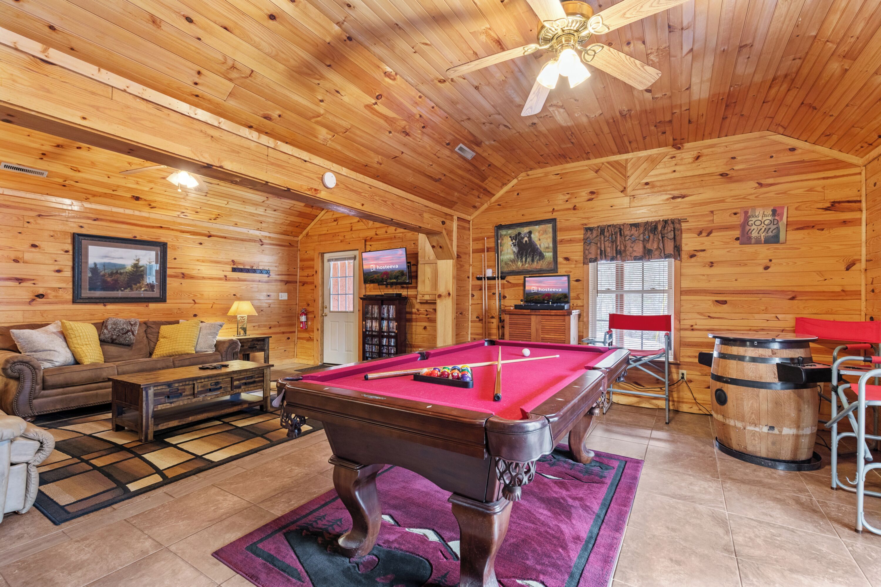 A wooden cabin interior with a pool table, a sofa, a television, and a fireplace.