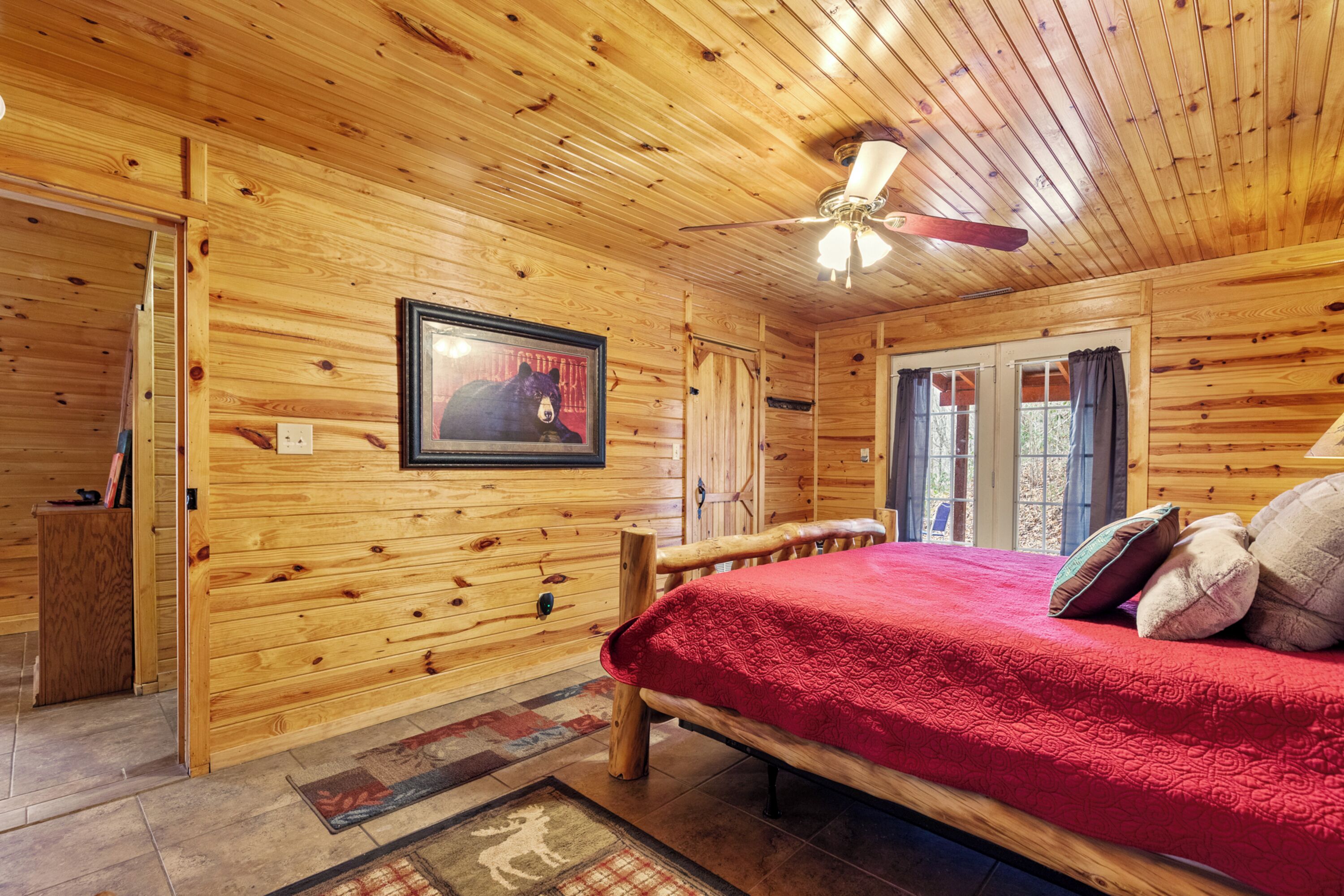 A wooden cabin bedroom with a bed, a ceiling fan, and a framed picture on the wall.