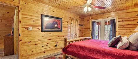 A wooden cabin bedroom with a bed, a ceiling fan, and a framed picture on the wall.