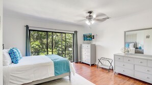 Un dormitorio con cama, cómoda, televisor y ventilador de techo.