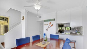 Un comedor con una mesa de madera, sillas azules y una cocina al fondo.