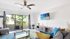 Una sala de estar moderna con un sofá gris, cojines coloridos, una mesa de centro y un televisor montado en la pared.