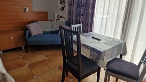 A small, cozy room with a bed, a sofa, a table with a tablecloth, a chair, and a window with curtains. - Chez Anabel & Stéphane (Battenheim)
