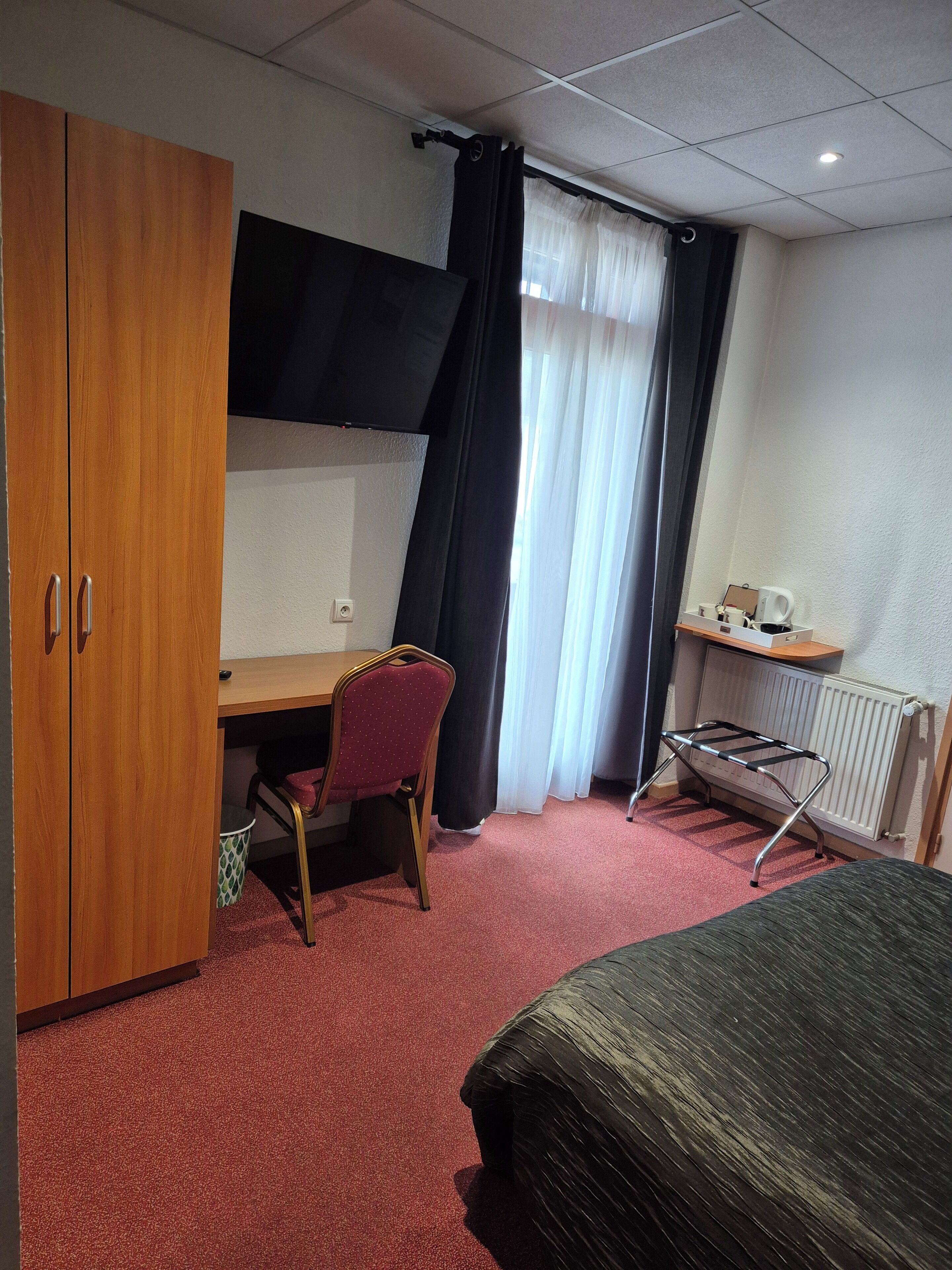 Ein Hotelzimmer mit Holzschrank, Schreibtisch, Stuhl, Heizkörper und Bett.