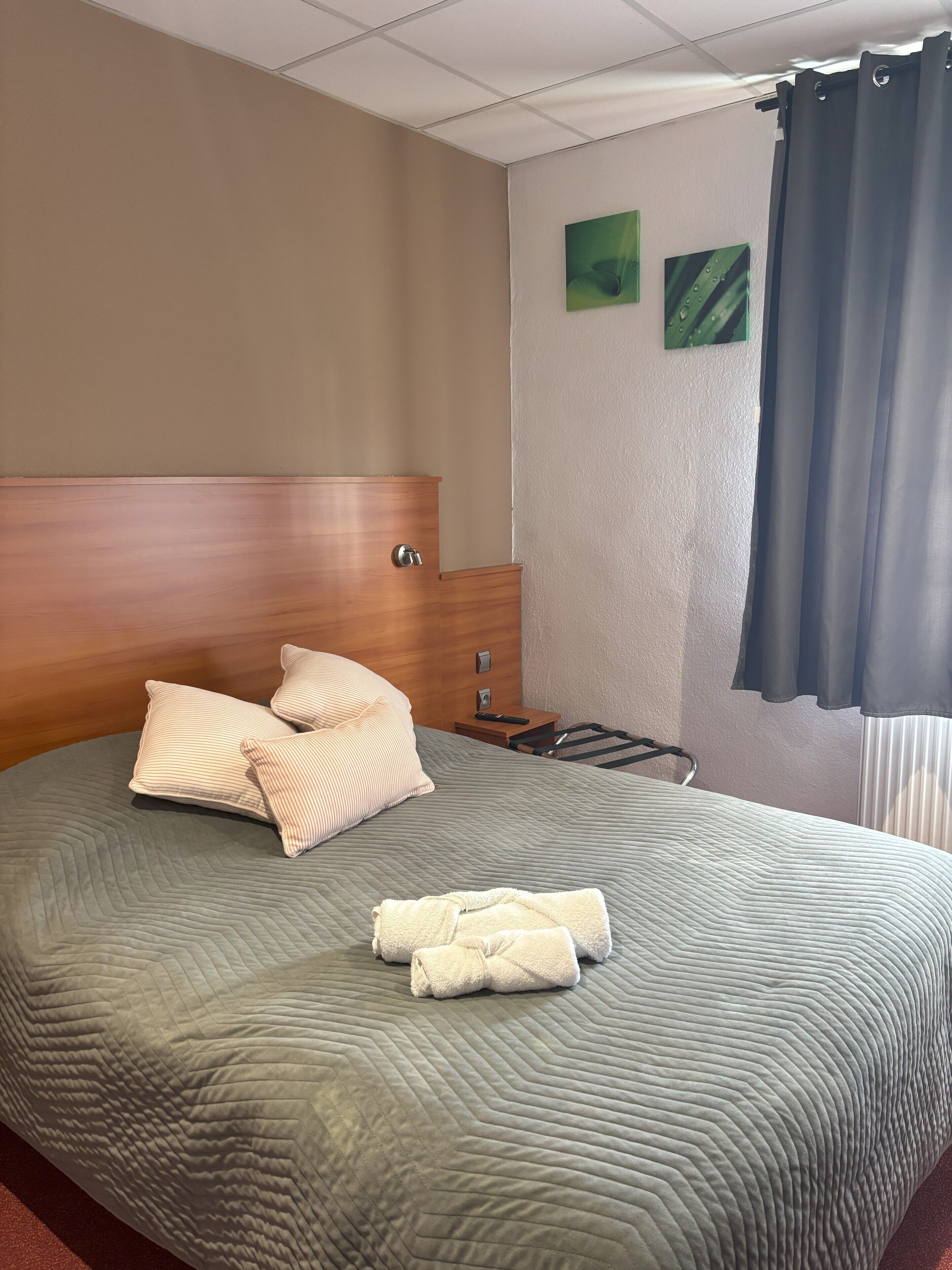 Una cama bien hecha con almohadas, un cabecero de madera y una mesita de noche con un control remoto.