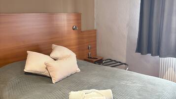 Una cama bien hecha con almohadas, un cabecero de madera y una mesita de noche con un control remoto.