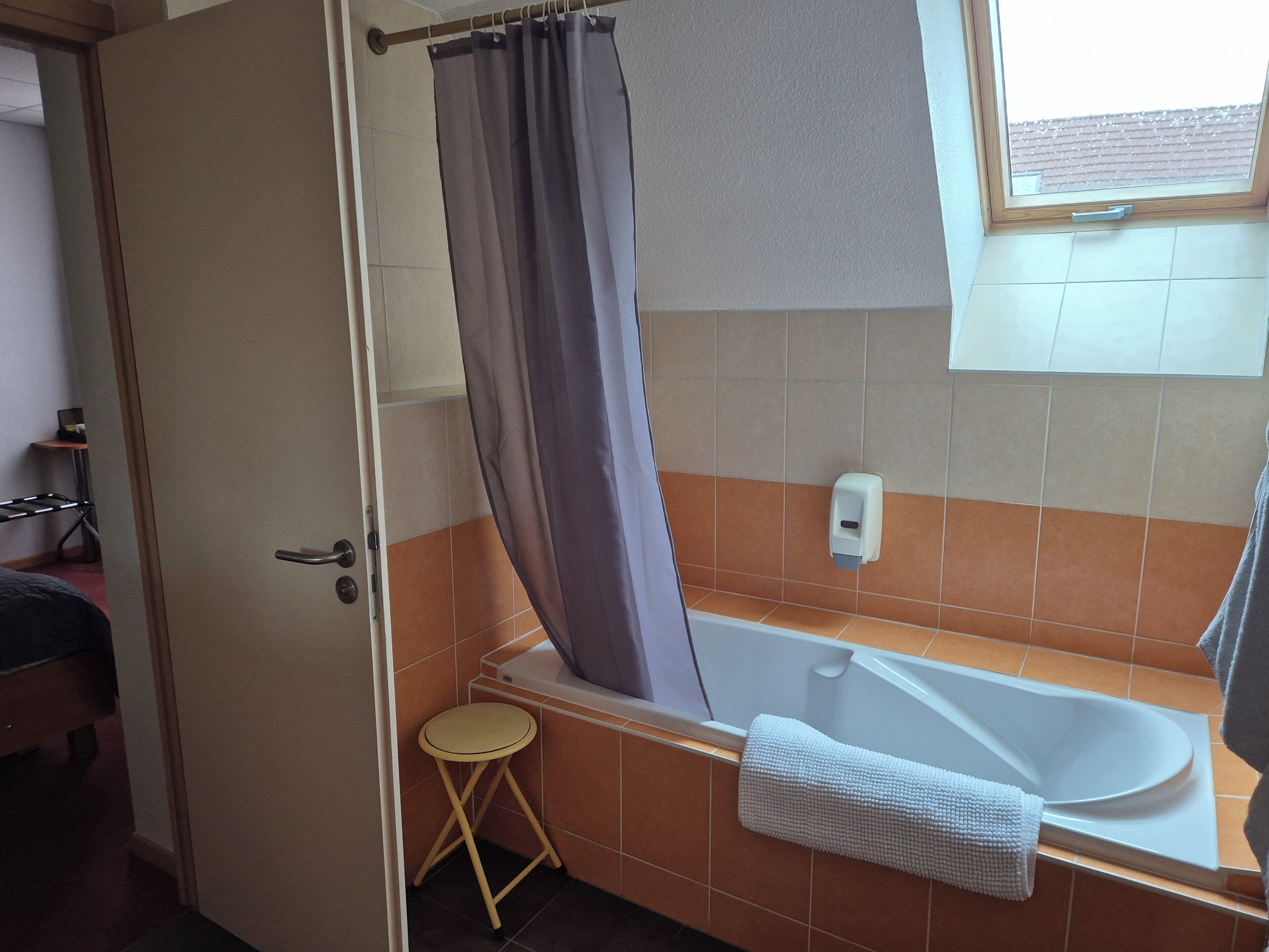 A bathroom with a bathtub, a shower curtain, a small stool, and a towel rack.