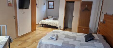 A hotel room with a large bed, a smaller bed, a TV, and a table with a chair.