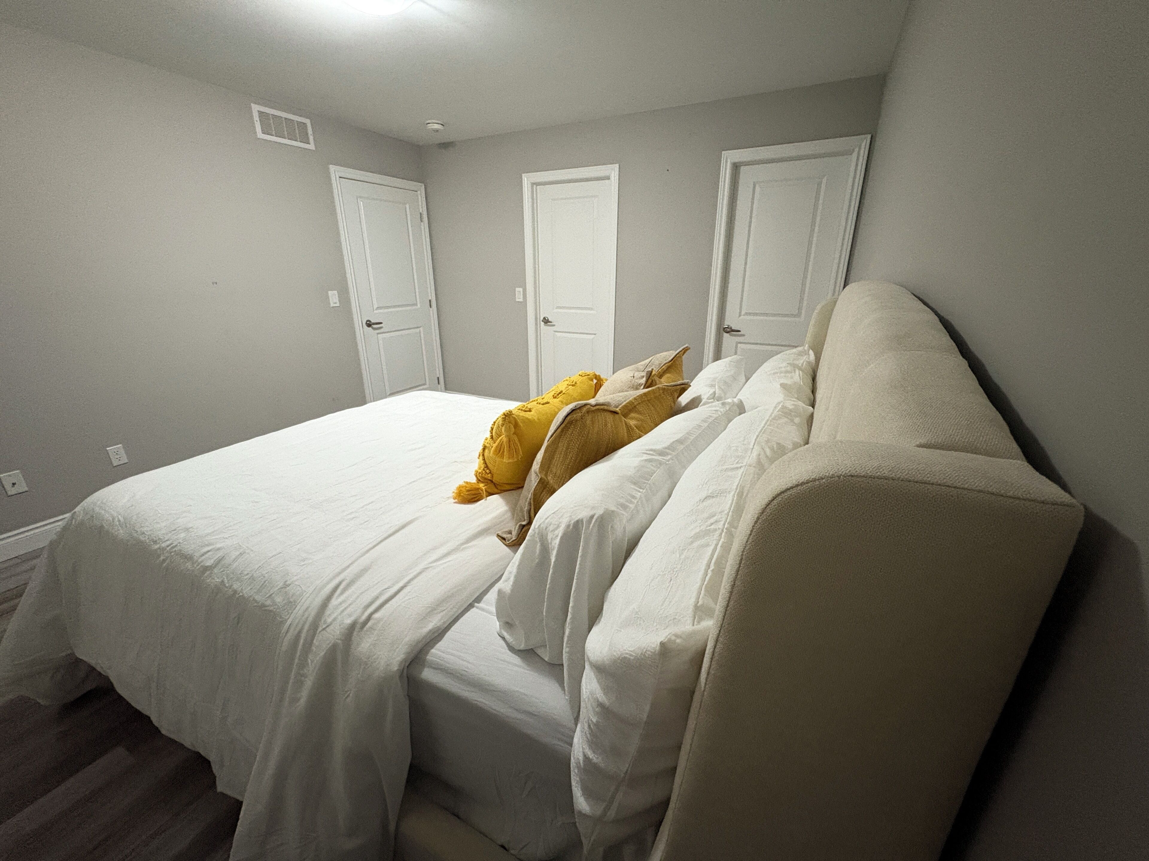 Een slaapkamer met een bed, witte muren en drie witte deuren.