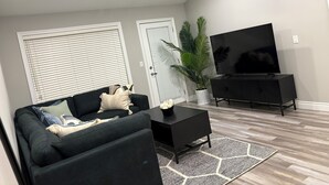 Un saló modern amb un sofà fosc, una taula de cafè negra, un gran televisor de pantalla plana i una planta en test.