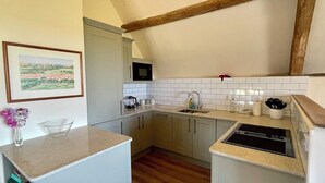 Cocina compacta con gabinetes blancos, microondas, lavabo y una viga de techo de madera.