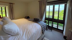 Un dormitorio con una cama grande, una mesita con una silla y vistas a un paisaje verde a través de la ventana.