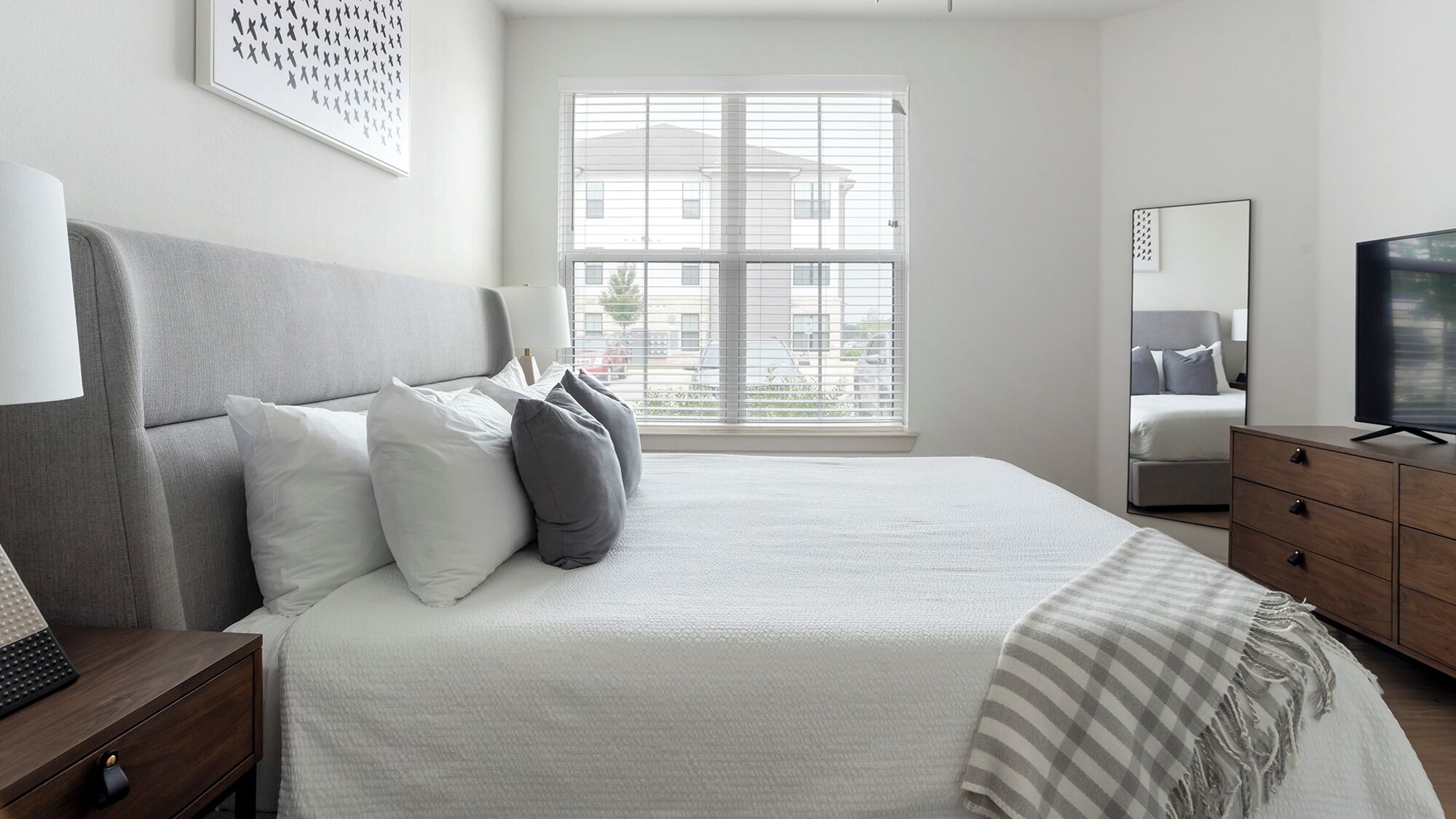 A modern bedroom with a large bed, a TV, and a window with blinds.