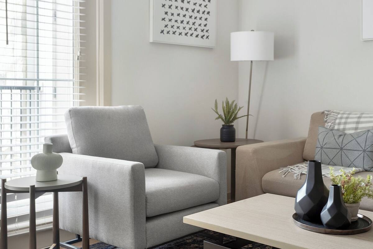Un salon moderne avec un canapé gris, une petite table d’appoint, un lampadaire et un vase décoratif.