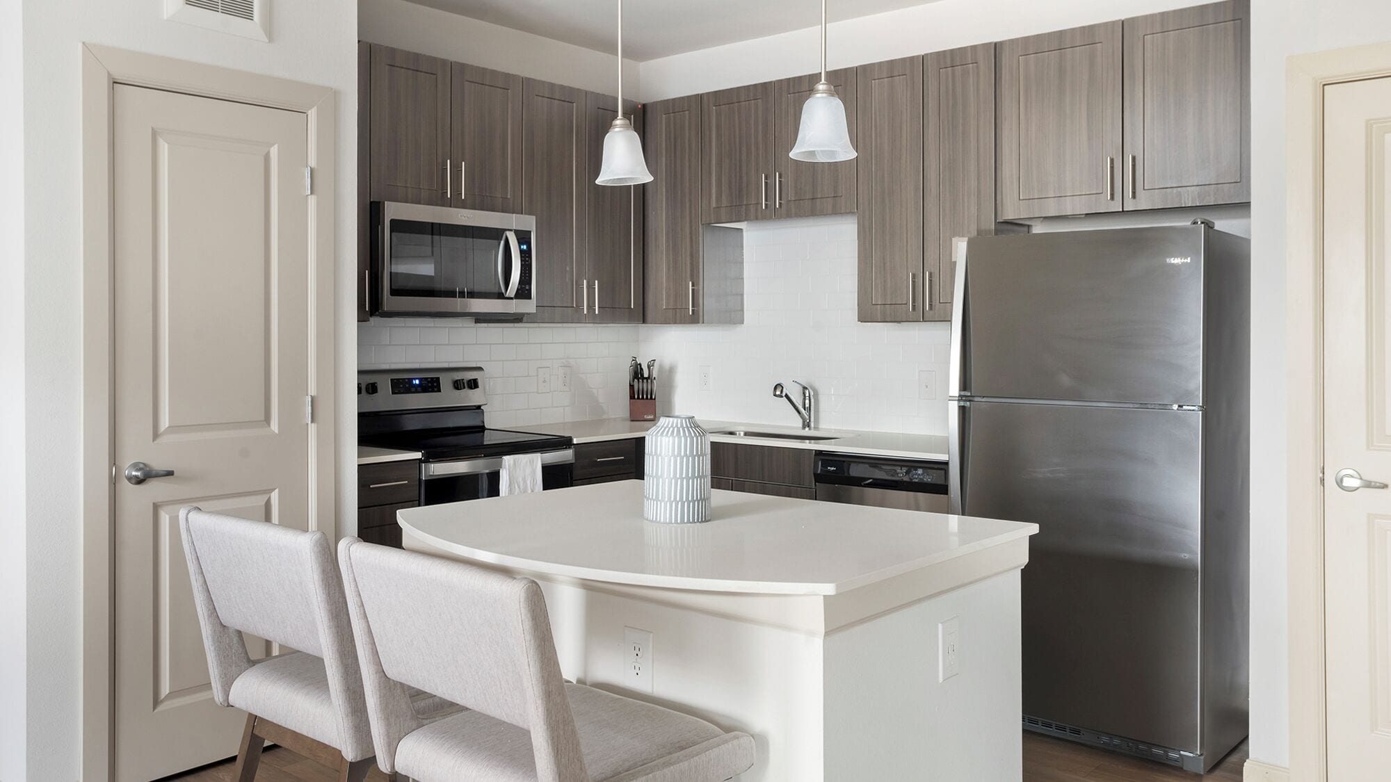 Une cuisine moderne dotée d’un îlot central, d’appareils électroménagers en acier inoxydable et de meubles de rangement en bois clair.