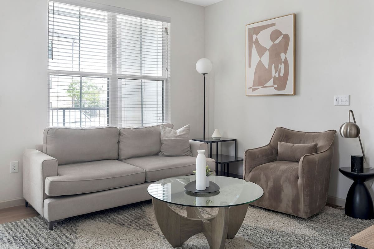 Un salon moderne avec un canapé beige, une table basse en verre, un lampadaire noir et un tableau accroché au mur.