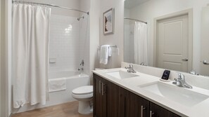A modern bathroom with a bathtub, toilet, and a double sink vanity.