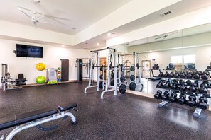 A gym with exercise equipment, a bench, a mirrored wall, and a television. - Landing Apartments Pflugerville (Pflugerville)