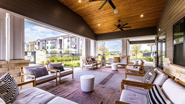 A covered outdoor seating area with wooden furniture and a ceiling fan. - Landing Apartments Pflugerville (Pflugerville)