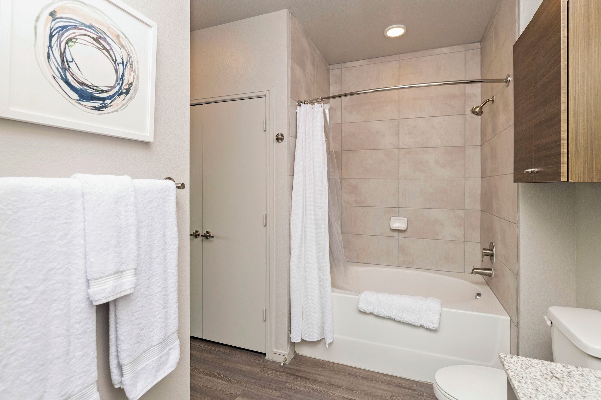 A modern bathroom with a bathtub, shower, and toilet. There are white towels on the floor and a shower curtain.