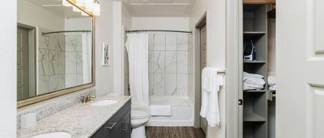 A modern bathroom with a marble vanity, a large mirror, a shower, and a walk-in closet.