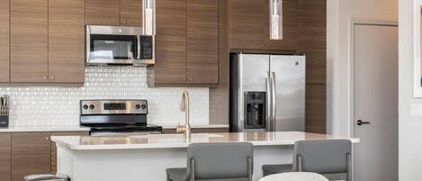 Cocina moderna con armarios de madera, electrodomésticos de acero inoxidable y una isla central con taburetes de bar.