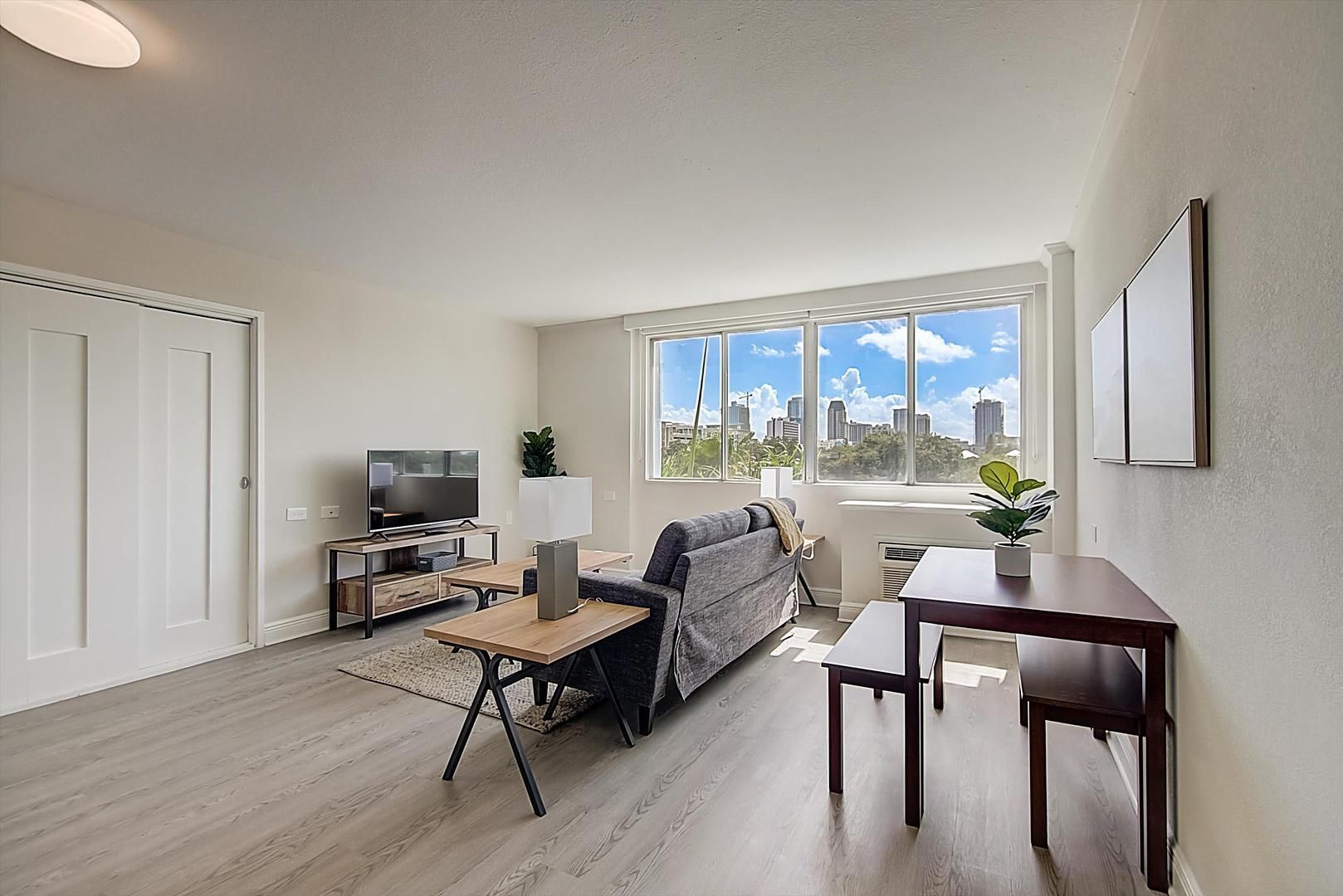 A modern living room with a sofa, TV, coffee table, and a large window with a city view.