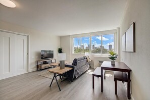 Ein modernes Wohnzimmer mit Sofa, Fernseher, Couchtisch und einem großen Fenster mit Blick auf die Stadt.