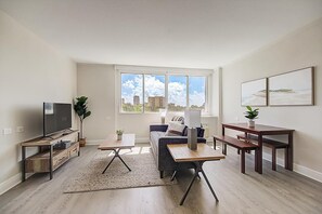 A modern living room with a flat-screen TV, a sofa, a coffee table, and a dining table. There is a large window with a view of buildings and a plant on the windowsill. - Landing St. Petersburg (St. Petersburg)