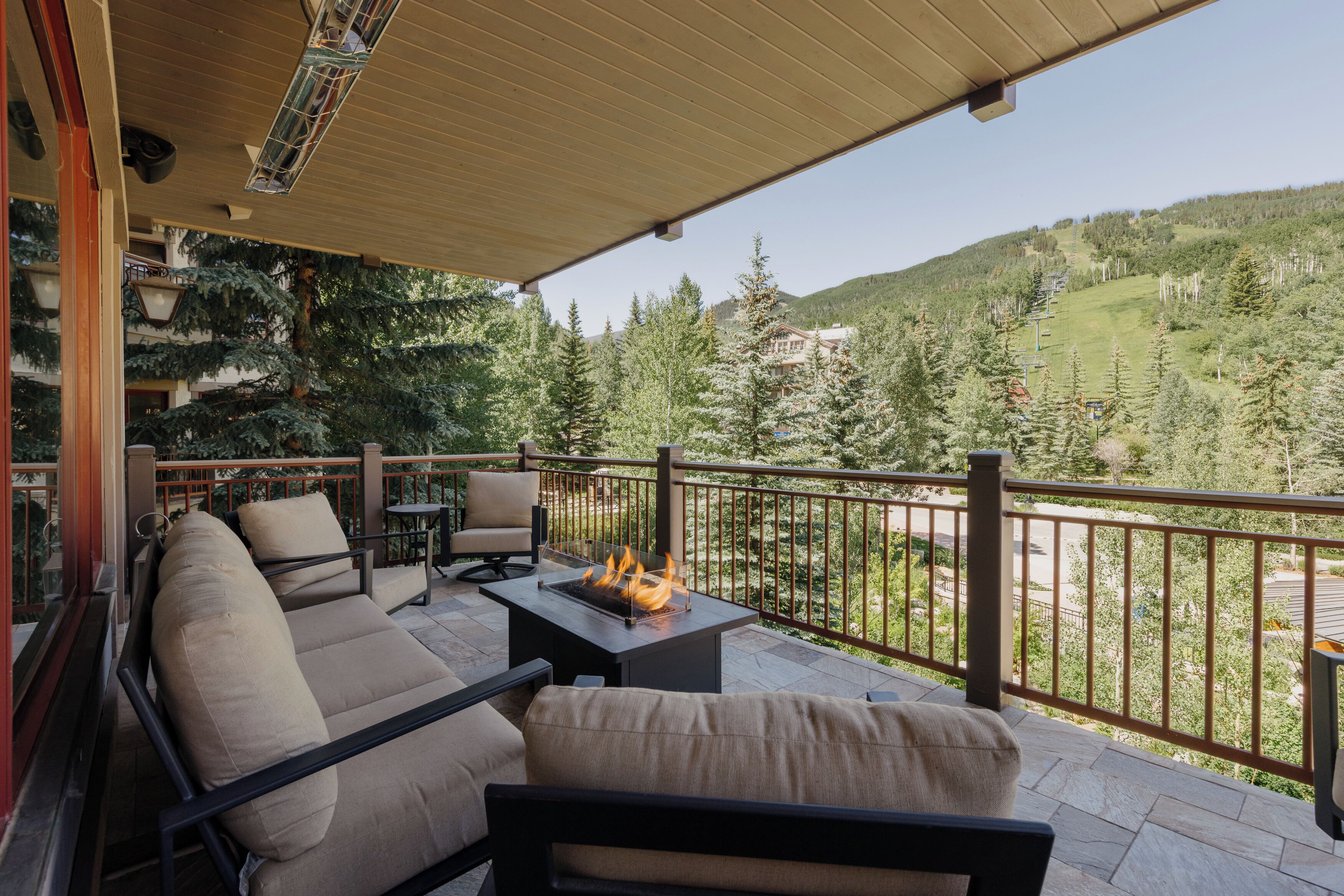 A covered outdoor seating area with a sofa and chairs, a fire feature, and a view of a mountainous landscape.