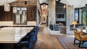 A spacious kitchen with a large island, stone accents, and modern lighting fixtures. - Luxe Estate by InvitedHome | Theater, Gym, Decks, Views, Hot Tub, Ski-In/Out (Park City)
