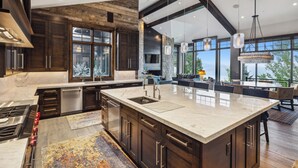 A modern kitchen with a large island, dark wood cabinets, and a stone accent wall. - Luxe Estate by InvitedHome | Theater, Gym, Decks, Views, Hot Tub, Ski-In/Out (Park City)