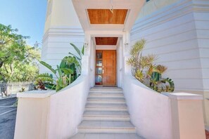 Stairs lead to a door flanked by potted plants and white walls.