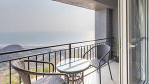 Un balcón con sillas de mimbre y una mesa de vidrio, con vista al mar.