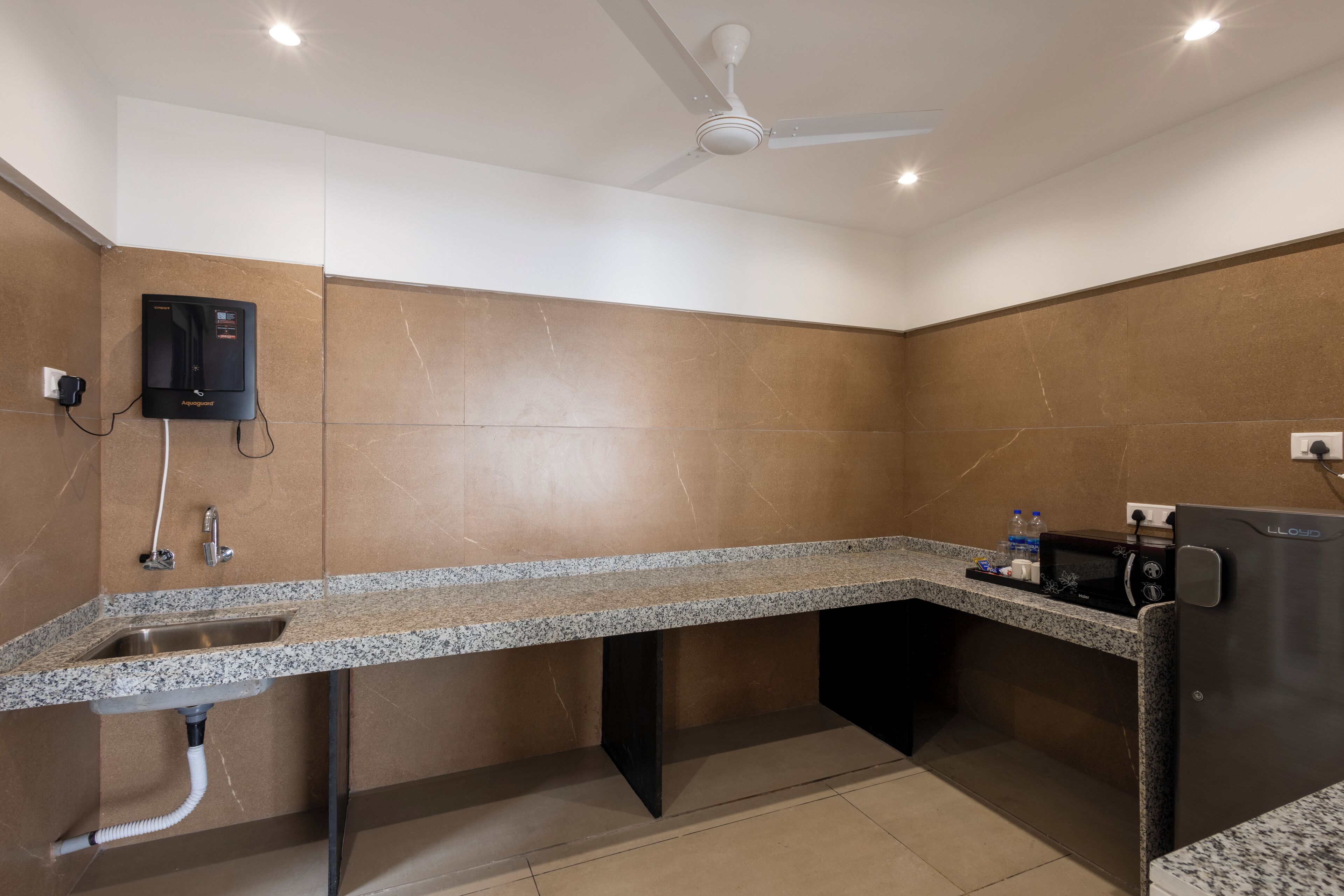 A modern bathroom with a granite countertop sink, a built-in heater, a ceiling fan, and a compact refrigerator.