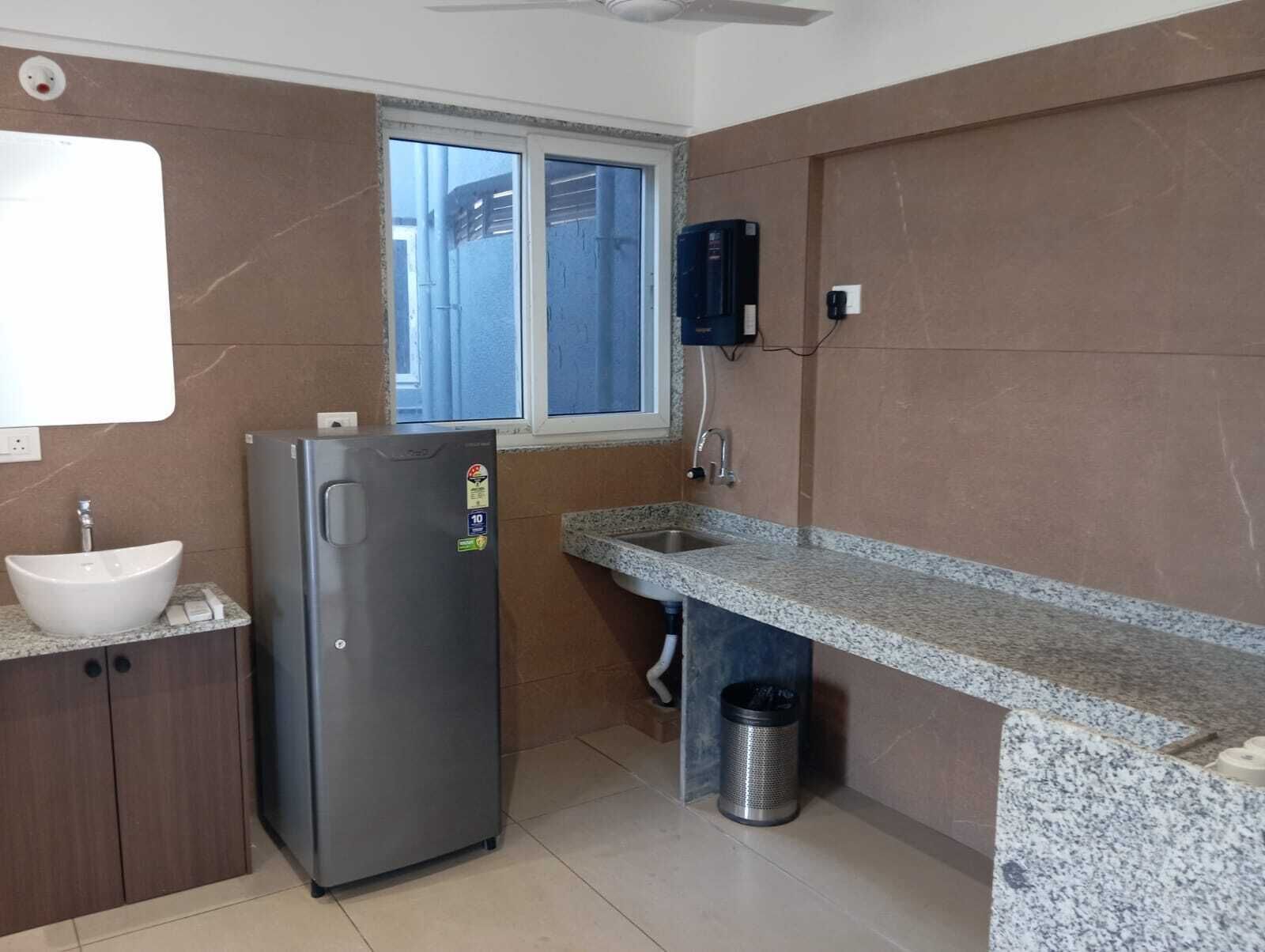 A compact kitchen with a built-in sink, a stainless steel refrigerator, and a window above the sink.