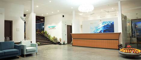A spacious lobby with a reception desk, seating area, and a staircase leading to upper floors.