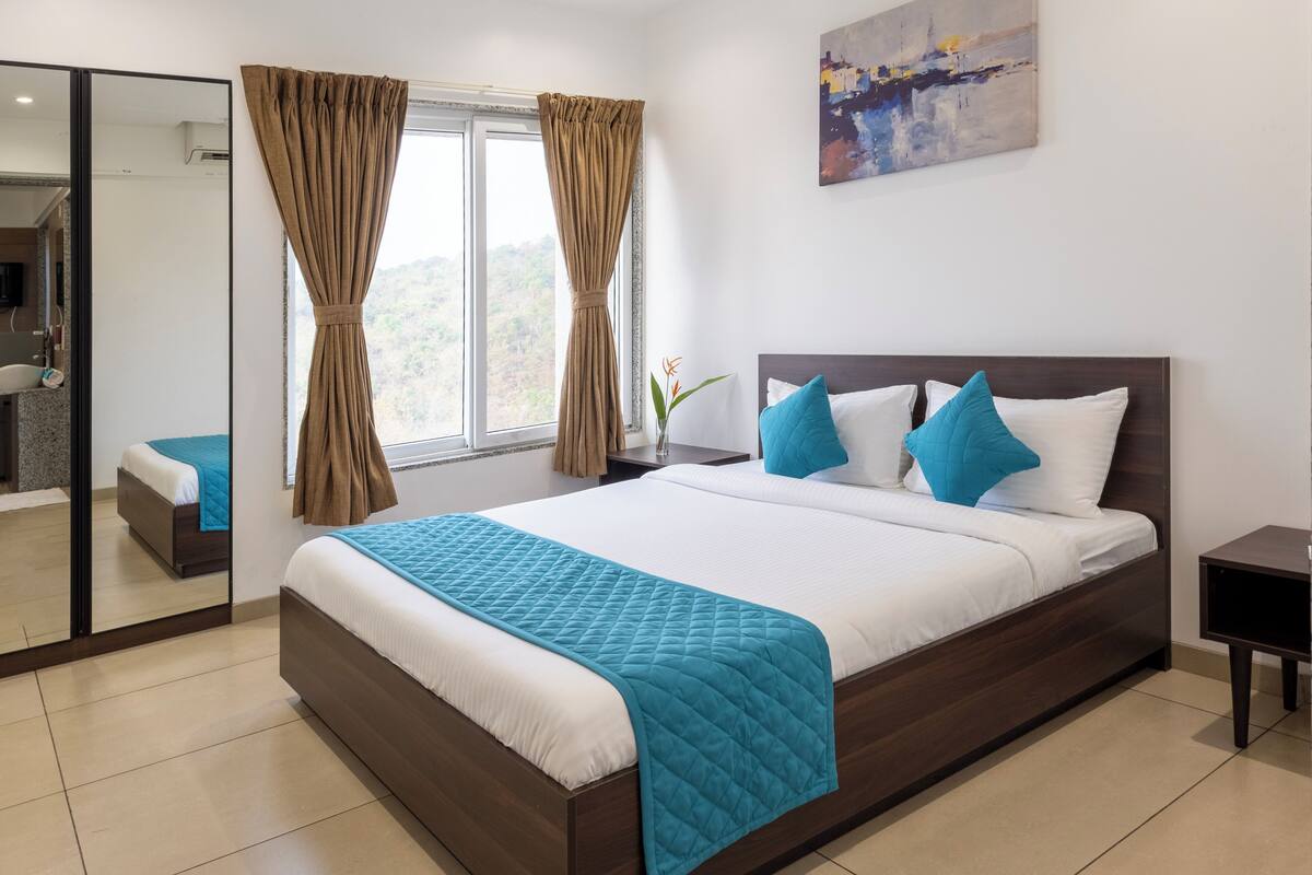 A modern bedroom with a large bed, a ceiling fan, a painting on the wall, and a view of the outdoors through the window.