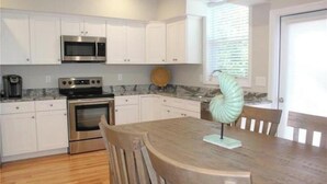 A kitchen with white cabinets, a stainless steel microwave, a double oven, and a dining table with chairs. - Modern Coastal Condo w/ Heated Pool Near Ogunquit & Wells Beach (Wells)