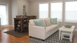 A living room with a sofa, a small table, and a bookshelf. - Modern Coastal Condo w/ Heated Pool Near Ogunquit & Wells Beach (Wells)