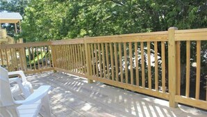 A wooden deck with a railing, white plastic chairs, and a view of trees and a building in the background. - Modern Coastal Condo w/ Heated Pool Near Ogunquit & Wells Beach (Wells)