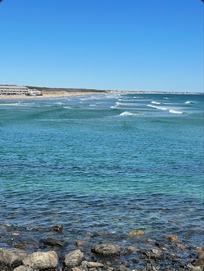 Une vue sur la côte, avec une eau limpide, un rivage rocheux et un bâtiment situé au loin.