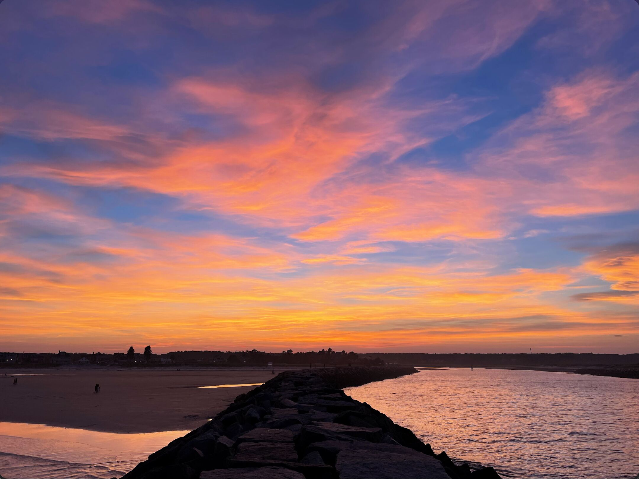 A sunset over a beach with a rocky breakwater.
