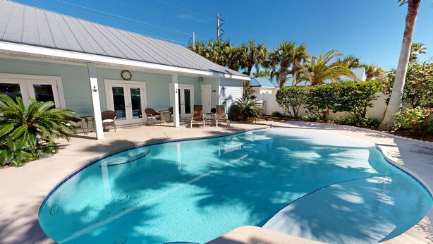 A swimming pool with lounge chairs, a covered patio, and palm trees.